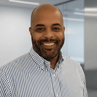 Foto de rosto de Giovani sorrindo, com barba e camisa social listrada